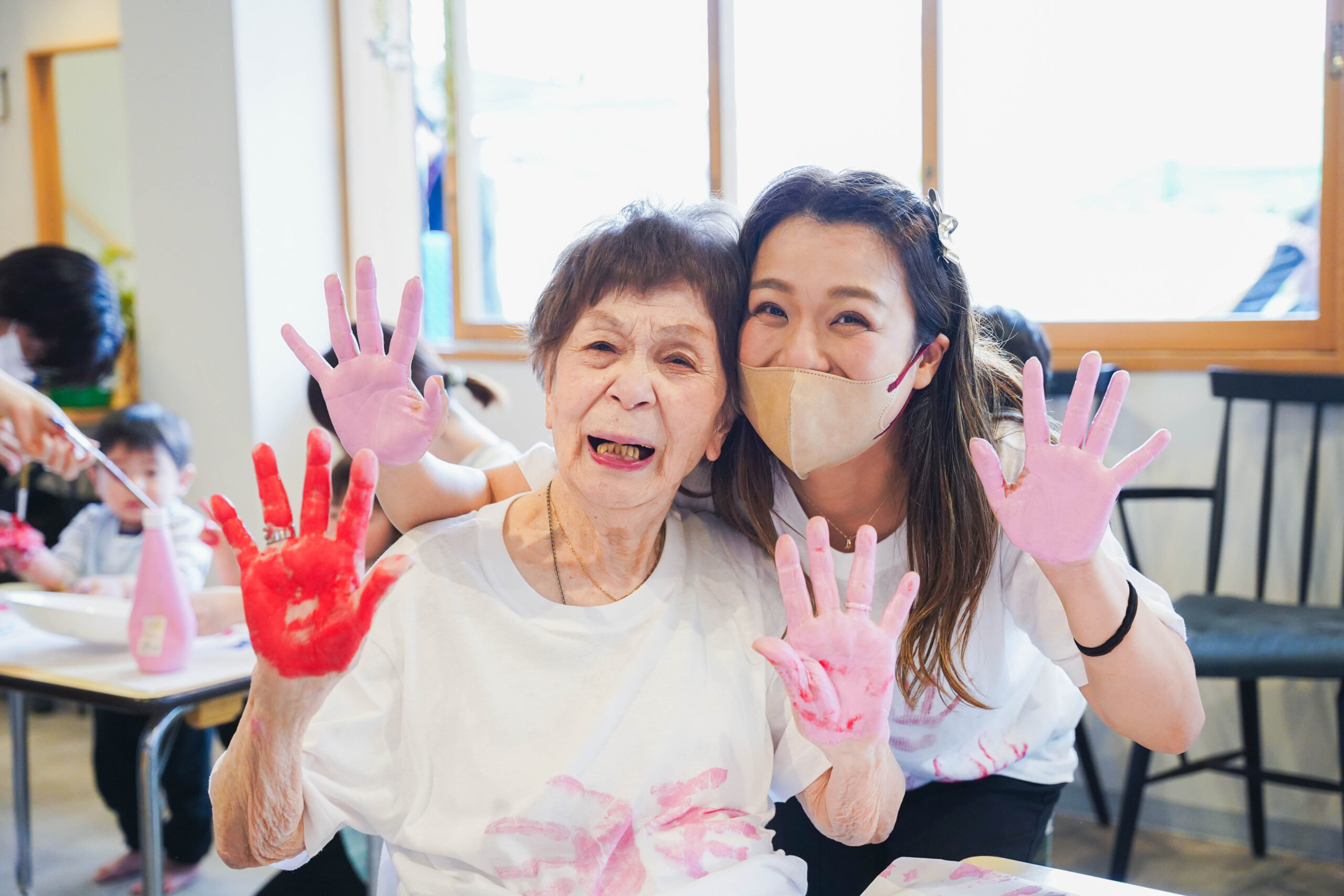 両手に絵の具を付けて笑顔で両手を見せるおばあちゃんと若い女性